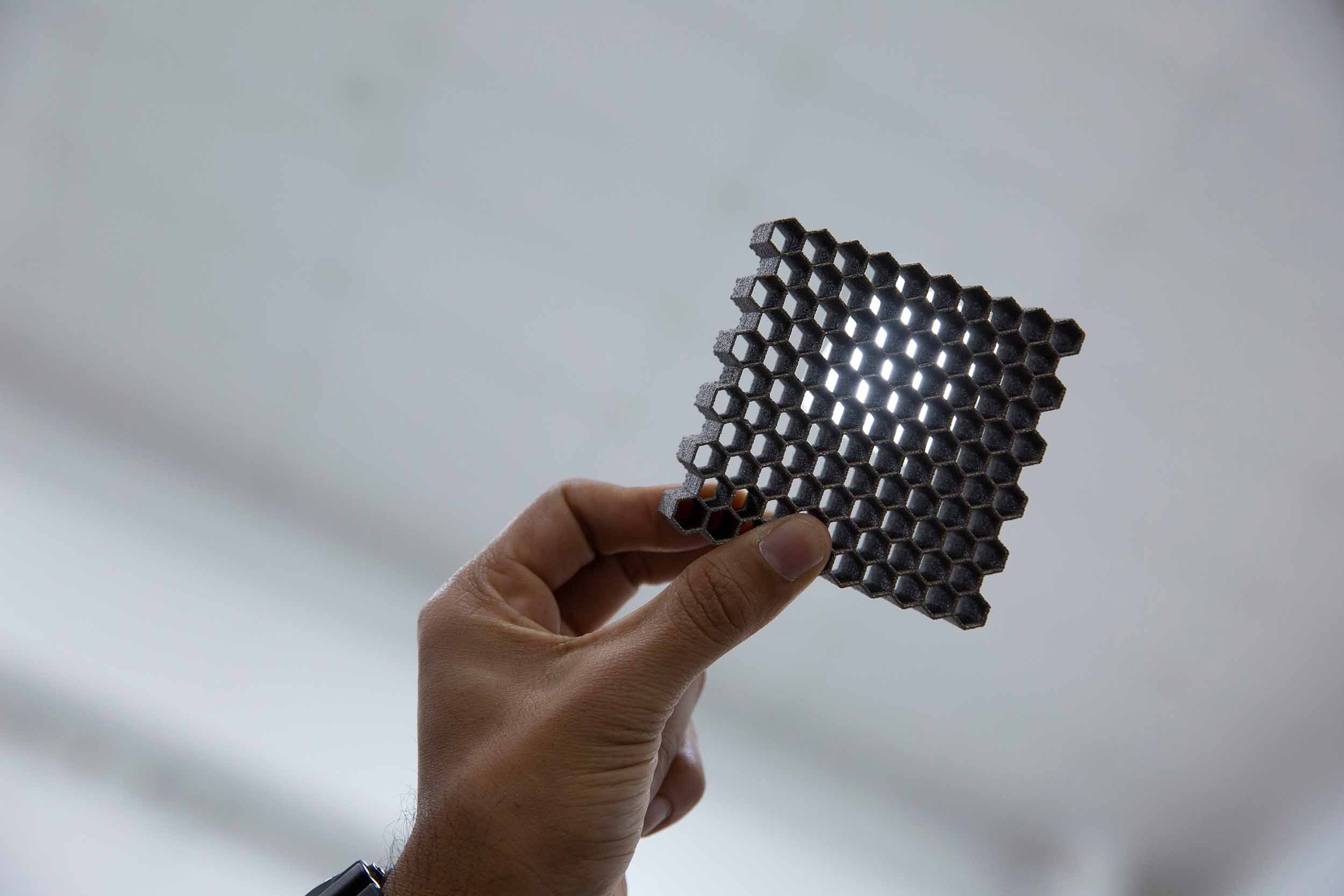 Dgruv Bhate holds up a sample of a 3D printed hexagon structure modeled after a beehive