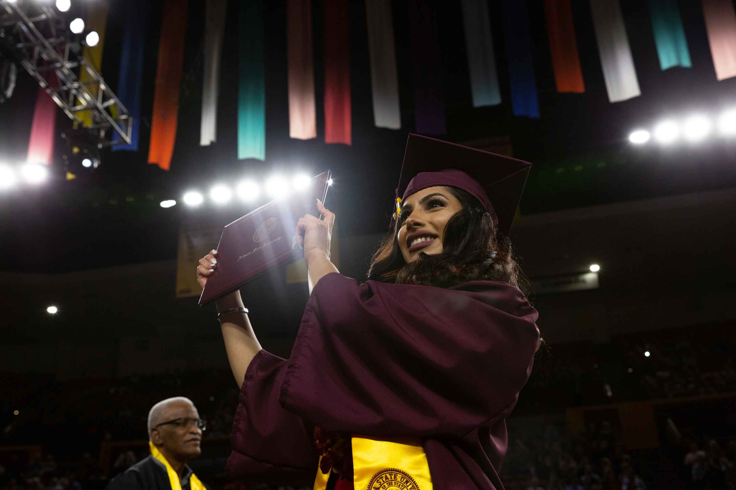 A graduate holds up her diploma, smiling, as she crosses the stage at the Fulton Schools Convocation