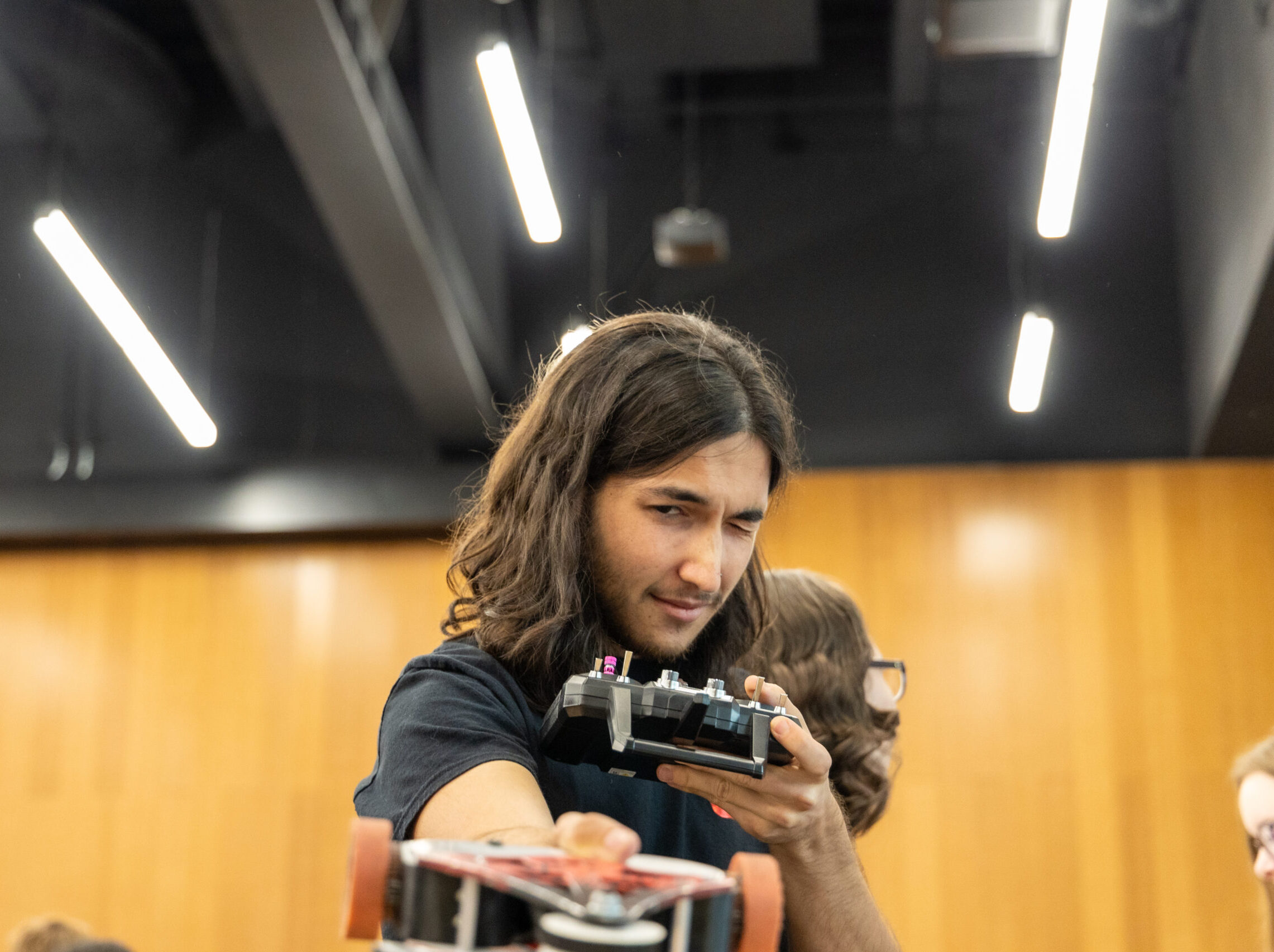 A student holds a device that looks like a game controller but is using it to eye up some kind of material he's observing in the foreground.