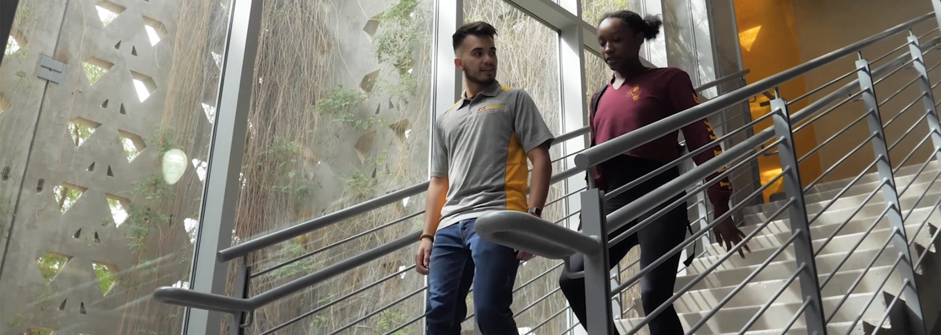 Male and female student walking down a staircase and chatting.