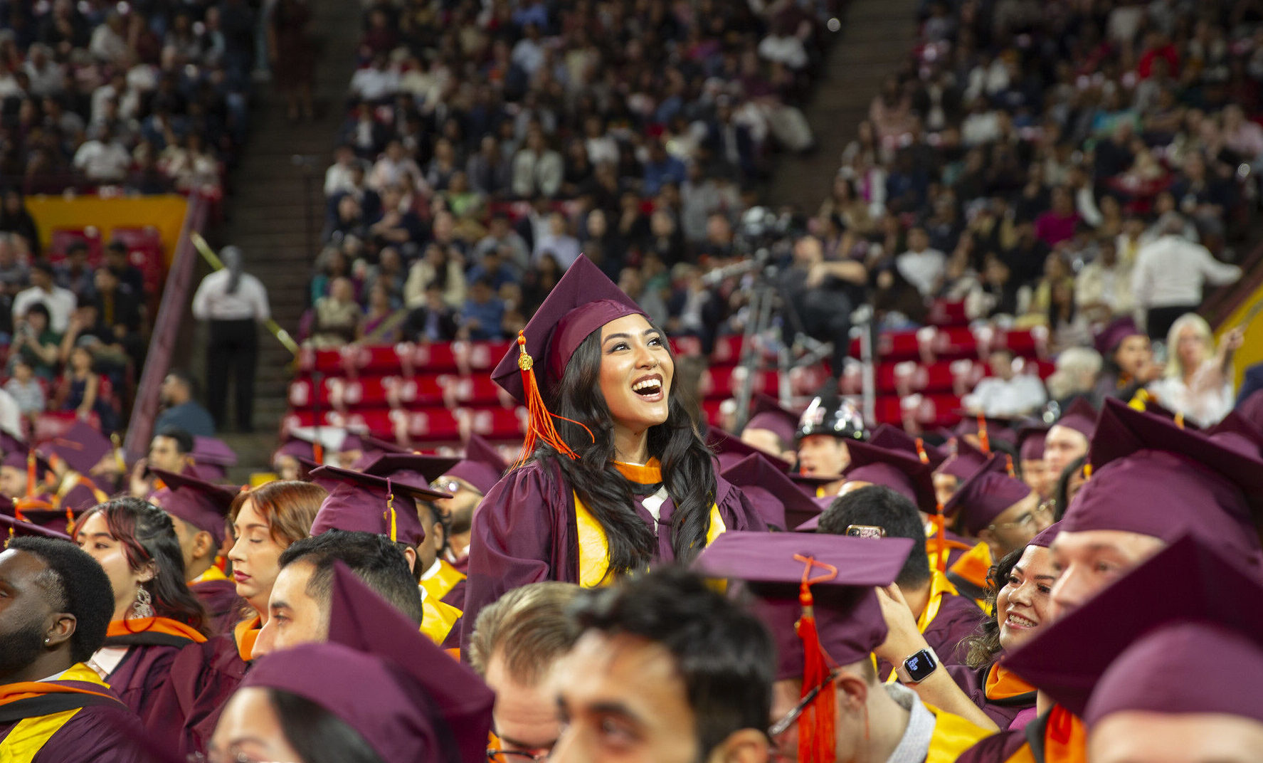 A female student stands and waves at her family and friends at the Fall 2024 undergraduate convocation. Photographer: Erika Gronek